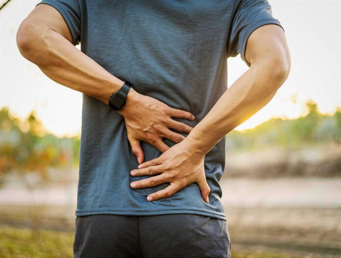 1020731773 Person holding lower back in discomfort outdoors