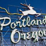 Neon sign reading Portland Oregon with a leaping deer against a blue sky