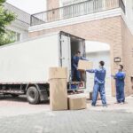 Workers unloading boxes from a moving truck in a residential driveway