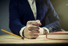 A man's clenched fist resting on a desk with office supplies nearby
