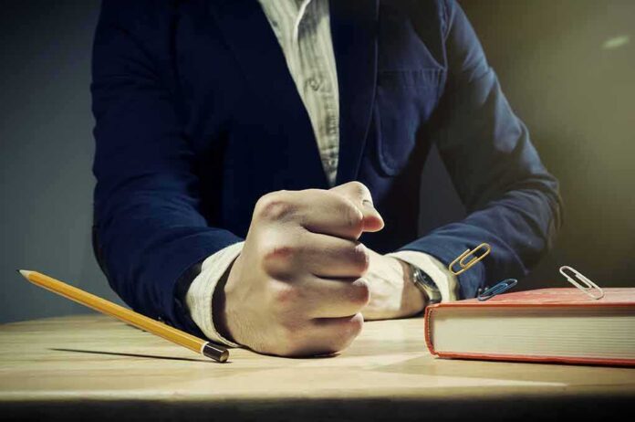 A man's clenched fist resting on a desk with office supplies nearby