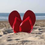 Red flip flops resting in the sand with an ocean background