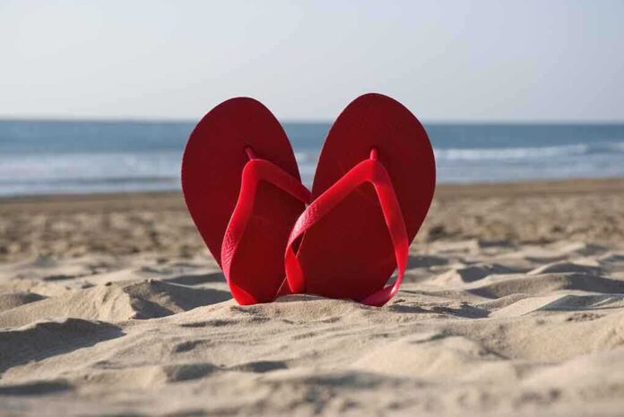Red flip flops resting in the sand with an ocean background
