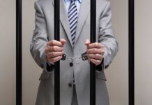 Anti-Corruption Hero BUSTED—Massive Bribe Bombshell Businessman in a suit holding prison bars with handcuffs on his wrists