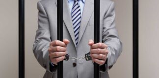 Businessman in a suit holding prison bars with handcuffs on his wrists