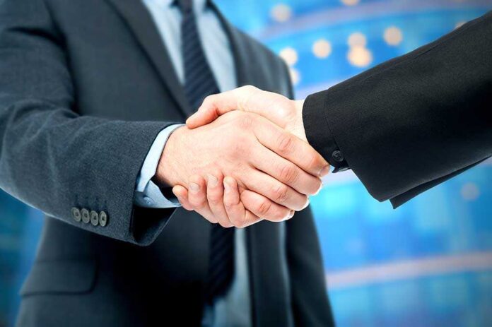 shutterstock_174221906.jpg Two business professionals shaking hands in a corporate setting
