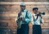 Two jazz musicians playing saxophone and trumpet against a wooden wall