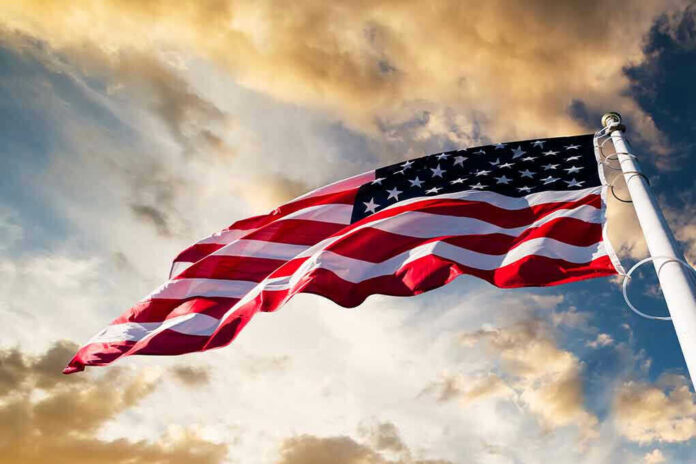 360951227 American flag waving against a cloudy sky.