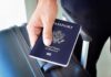 A person holding a United States passport next to a suitcase