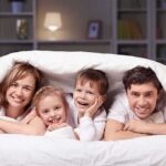 A family of four smiling and cuddling under a blanket