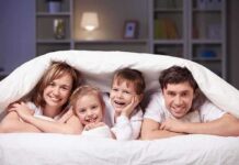 A family of four smiling and cuddling under a blanket
