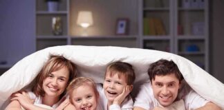 A family of four smiling and cuddling under a blanket