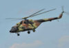 Camouflage military helicopter in flight against blue sky.