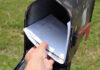 Postmaster’s Plan: Stamps to Hit $1? Hand placing mail in a black mailbox.