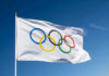 Olympic flag waving against clear blue sky.