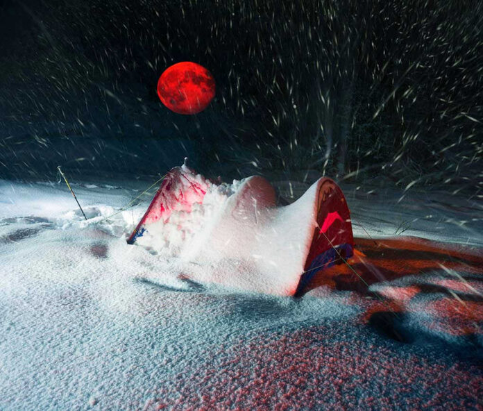 773702869 Red moon above snowy tent in blizzard night
