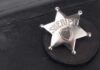 A silver sheriff badge resting on a black leather surface