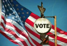 A vintage Vote sign in front of an American flag