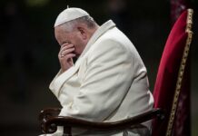Pope sitting with his head bowed and hand covering his face