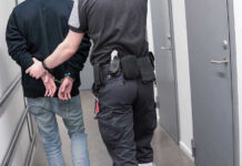 Crypto Plot To Attack LA Jewish Center EXPOSED Officer escorting handcuffed person down hallway.
