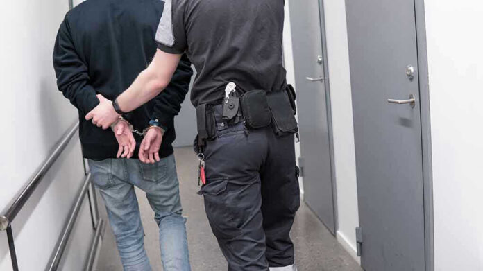1082126789 Officer escorting handcuffed person down hallway.