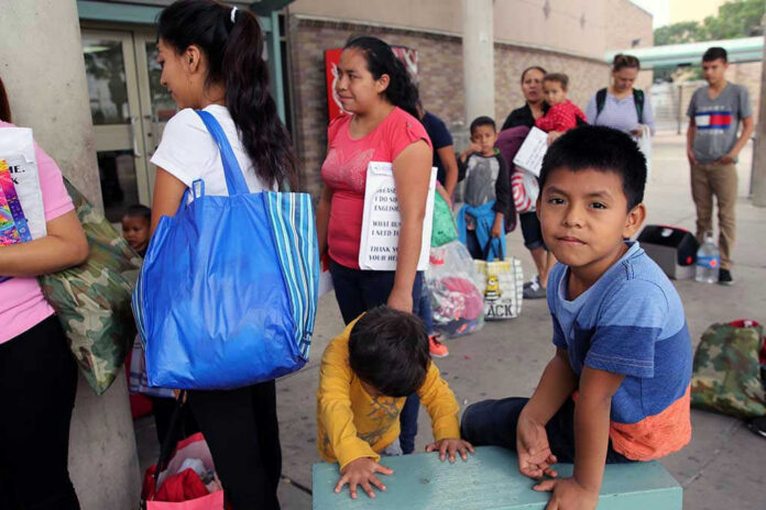 1378764938 People waiting outside carrying bags, boys sitting and playing.