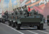 Tanks with military personnel in street parade formation.