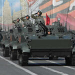 Tanks with military personnel in street parade formation.