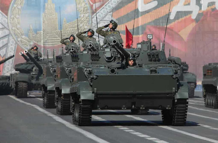Tanks with military personnel in street parade formation.