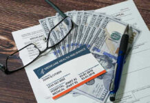 Medicare card glasses pen money on wooden table