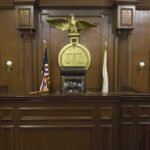 Appeals Court CRUSHES Trump’s $83M Defense Interior of a courtroom featuring a judges bench and American flag