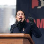 AOC Blasts Marjorie Taylor Greene as ‘Bigot’ – Alliance Debate Explodes A woman passionately speaking at a podium during a rally