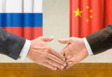 Two hands shaking in front of Russian and Chinese flags