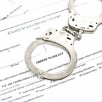 Councilman in Cuffs—The Vetting Failure Handcuffs on top of an arrest warrant document.