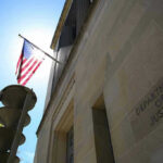 Citizenship Crackdown Explodes — Who’s Next? American flag at Department of Justice building exterior.