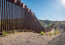 Border Wall Ultimatum Hits Texas Tall metal border wall with rural landscape.