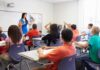 School Demographics Flip — Guess Who Shrank Teacher in a blue dress instructing students in a classroom with hands raised