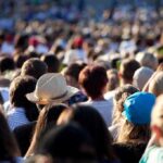 Chaos Erupts at TPUSA Summit A large crowd of people gathered outdoors, with various hats and hairstyles visible