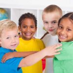 Hundreds Of Kids Vanish — What ICE Missed Four children of diverse backgrounds smiling and hugging each other in a classroom