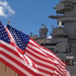 Barracks Horror Exposed — System Shrugged American flags in front of a naval ship under a blue sky
