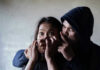Man holding womans mouth, gesturing silence.