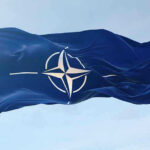 Kill List Drama Ignites NATO Presser NATO flag waving against blue sky.