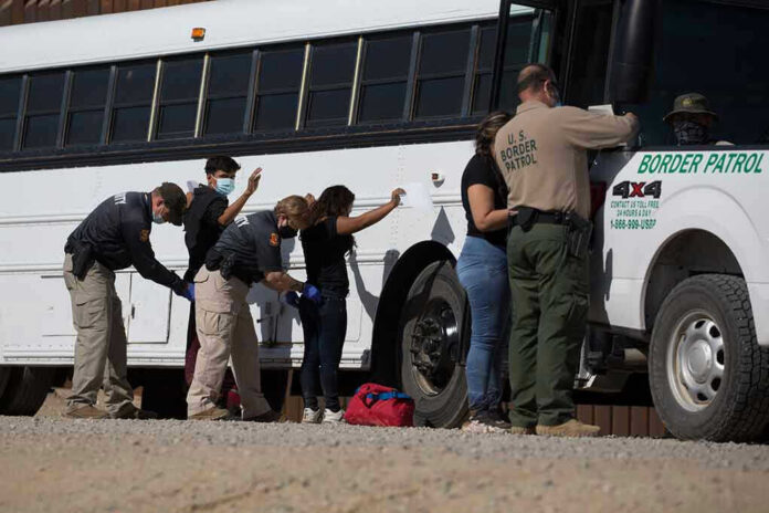 1973414852 Border patrol officers investigating people near a bus.