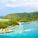 Epstein Island Revelations — Ominous, Incomplete Tropical beach with docks and lush green hills.