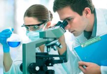 Child’s ‘Fatal’ Tumor Vanishes — Stuns Doctors Two scientists conducting an experiment in a laboratory, one looking through a microscope and the other holding a flask with blue liquid