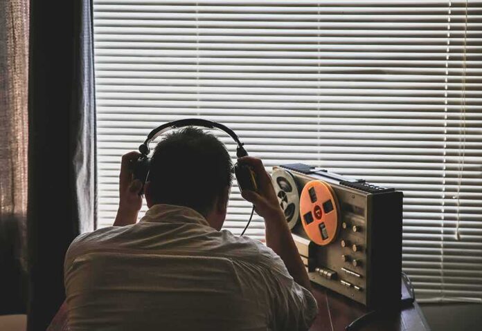 shutterstock_1478666012 Person wearing headphones listening to a reel-to-reel tape recorder