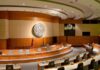 White House Firebrand Drops ‘Communist’ Bomb Interior view of a government chamber with wooden paneling and seating