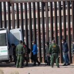 Cartel Crackdown Explodes — 478 Nabbed Border agents escort a group near a tall fence and a patrol van