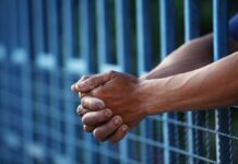 Close-up of clasped hands resting on a blue fence