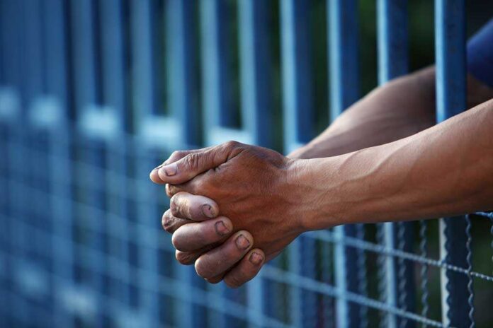 Hand,In,Jail Close-up of clasped hands resting on a blue fence